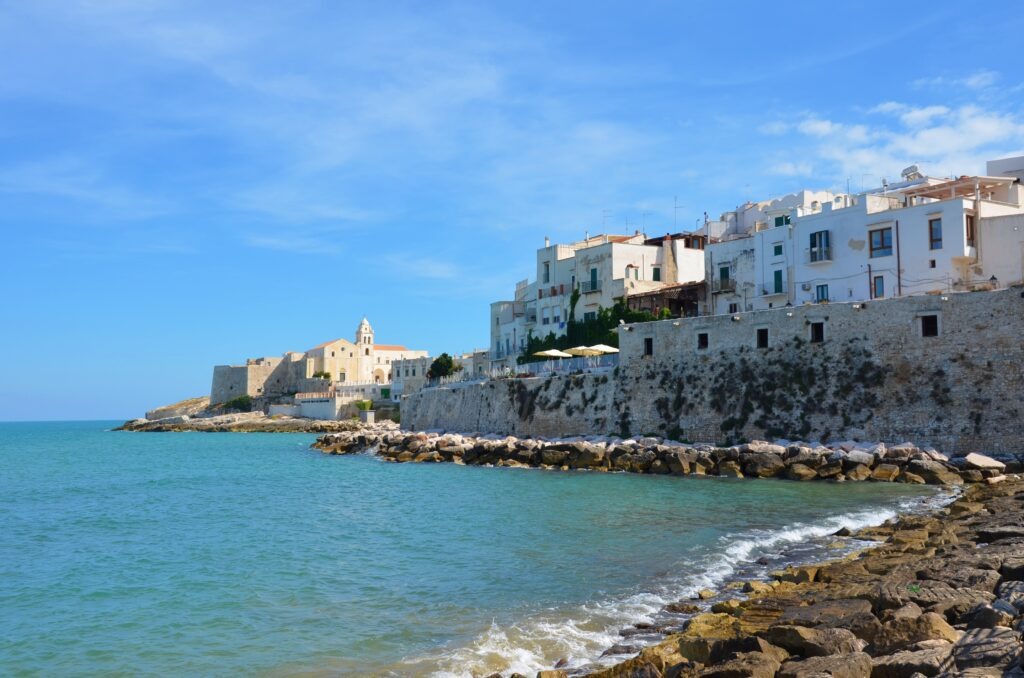 White historic buildings of Vieste built on a stone cliff overlooking the Adriatic Sea under a blue sky, Puglia, Italy."