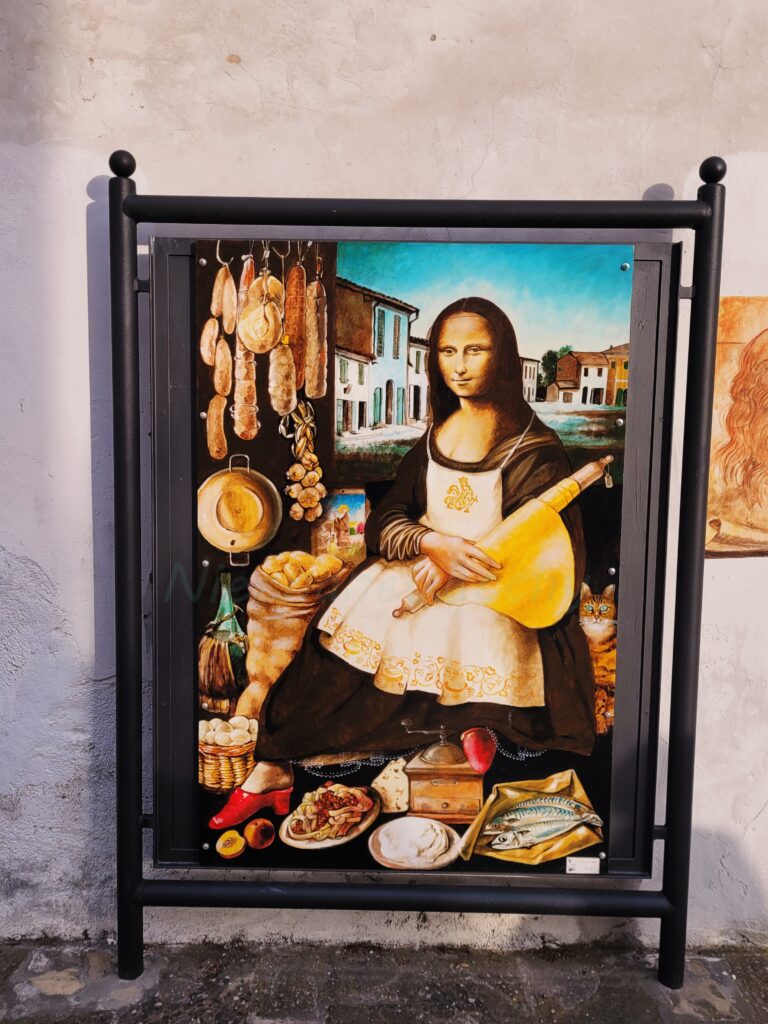 Street art z parodią Mony Lisy w fartuszku, otoczoną włoskimi produktami spożywczymi – wędlinami, serami, warzywami i rybą.