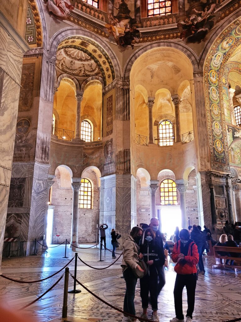 Wnętrze bazyliki San Vitale w Rawennie – tłum zwiedzających pod mozaikową kopułą i bogato zdobionymi arkadami
