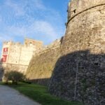 Potężne mury obronne i okrągła wieża Castello Angioino Aragonese w Agropoli. Widok z zewnętrznej ścieżki spacerowej na surową architekturę obronną zamku pod błękitnym niebem.