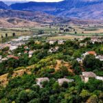 green hills covered with trees, among them you can see low houses with reddish-gray roofs
