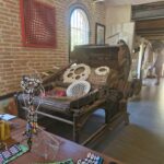 Interior of an art space with a large vintage machine decorated with circular patterned artworks, surrounded by colorful modern art pieces.
