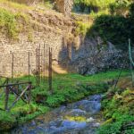 Clear stream flowing through a green valley with old stone walls and fences on the hillside above.