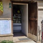 Small rustic shop with a wooden door open to reveal shelves of local products, and a handwritten menu board outside.