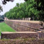 The long red brick defensive walls are surrounded by trees and grass.