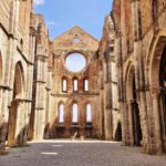 The ruins of an old monastery are in the center. Between the walls, you can see the front of the nave, which is pointed. It has longitudinal windows, with a round window at the top. The ruins have no roof.