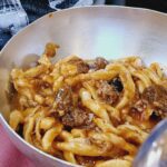 Thick spaghetti with meat in a silver metal bowl.