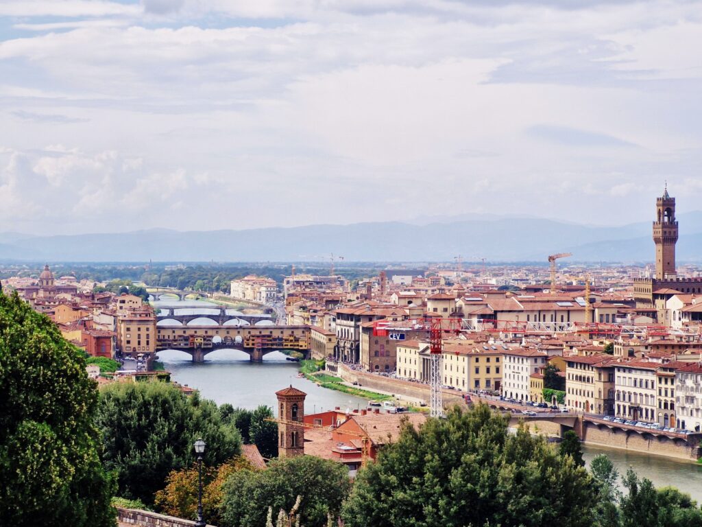 Trees grow on the banks of the river flowing under the bridges, and on one bank stand the buildings of Florence