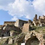 Ruins of an old hillside Craco with crumbling stone walls, arches, and collapsed buildings under a partly cloudy sky.