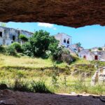 The old white houses of Ginosa stand behind the trees and grassy area of ​​Gravina di Ginosa.