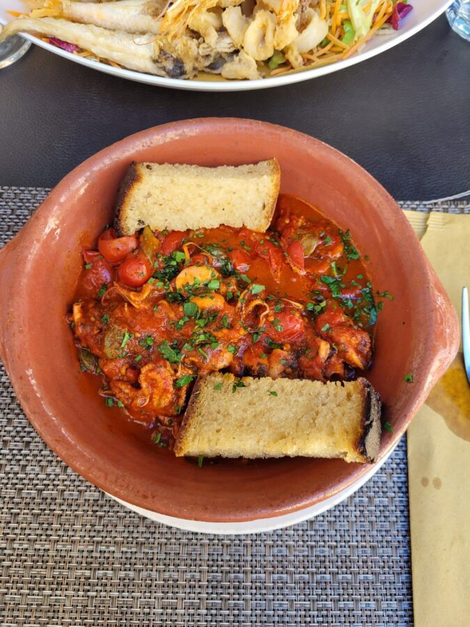 Baby octopus stewed in a rich tomato sauce with cherry tomatoes and fresh parsley, served in a traditional terracotta bowl with two slices of toasted bread.
