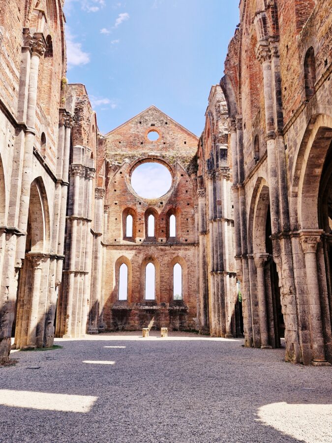 Wnętrze ruin opactwa San Galgano w Toskanii z ceglaną ścianą, pustą rozetą i kamiennymi kolumnami bez dachu