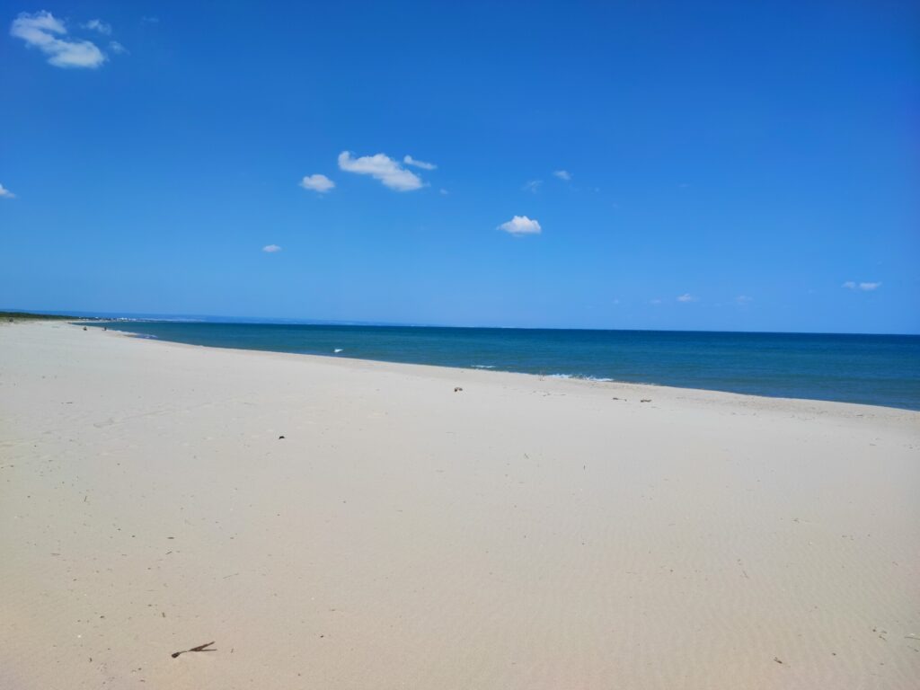 Apulia poza szlakiem. Wide, empty sandy beach stretching along the deep blue sea under a clear sky near Marina di Ginosa, Puglia.