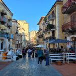 Historic stone gateway (Porta Monumentale) leading to the old town of Agropoli, Italy, with steps, visitors walking through the arch, and buildings under a clear blue sky.