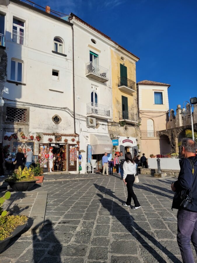 Paved town square with shops, white and yellow buildings, and visitors walking in the historic borgo of Agropoli, Campania