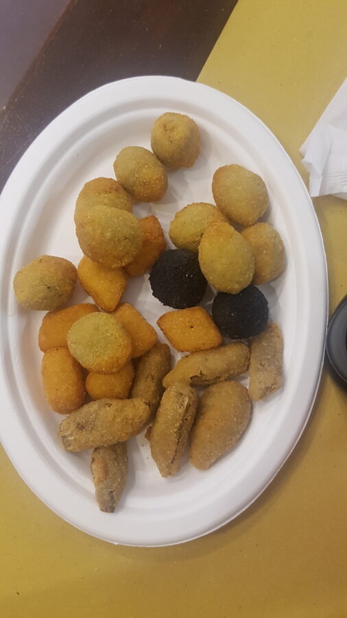 Porcja różnych rodzajów oliwek po askolańsku (olive all'ascolana) smażonych w głębokim tłuszczu, podana na białym, owalnym talerzu. Na porcję składają się panierowane oliwki w tradycyjnej, jasnej panierce o okrągłych, owalnych i lekko spłaszczonych kształtach oraz dwie oliwki w charakterystycznej, czarnej panierce.