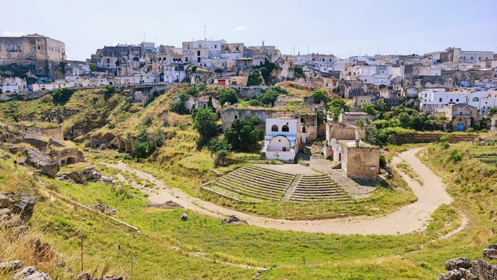 Apulia poza szlakiem. Panoramiczny widok na białe domy i osadę jaskiniową w Ginosa wybudowane na krawędzi wąwozu oraz kamienny amfiteatr na dnie doliny w Apulii.