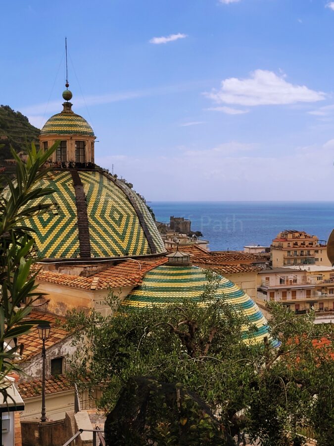 Domes of the Collegiata di Santa Maria Maddalena in Atrani, covered in green and yellow majolica tiles, overlooking the Mediterranean Sea.