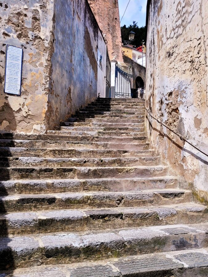 Narrow stone staircase ascending between weathered, rustic building walls along the Sentiero dei Limoni path on the Amalfi Coast.
