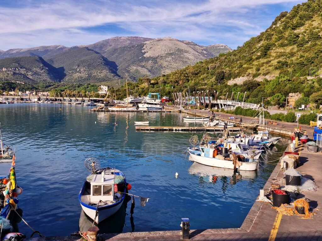 Small fishing boats moored along the pier at the port of Sapri, with fishing nets on the quay and coastal mountains in the background, hiking in Cilento, Campania, Italy.