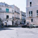 Białe domy stoją przy placy wyłożonym jasnym kamieniem.