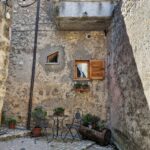 Small stone courtyard with a table, two chairs, and potted plants.