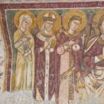 Ancient fresco depicting three haloed figures — a woman, a bishop holding a book, and an angel with wings — in vibrant medieval colors.