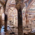 What to see near Rome.Interior of a medieval crypt with frescoed arches, stone columns, and intricate mosaic floors. Description: The image captures the richly decorated interior of an ancient crypt. The vaulted ceiling