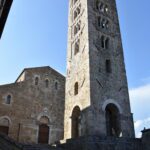 Tall medieval stone bell tower with arched windows against a clear blue sky.