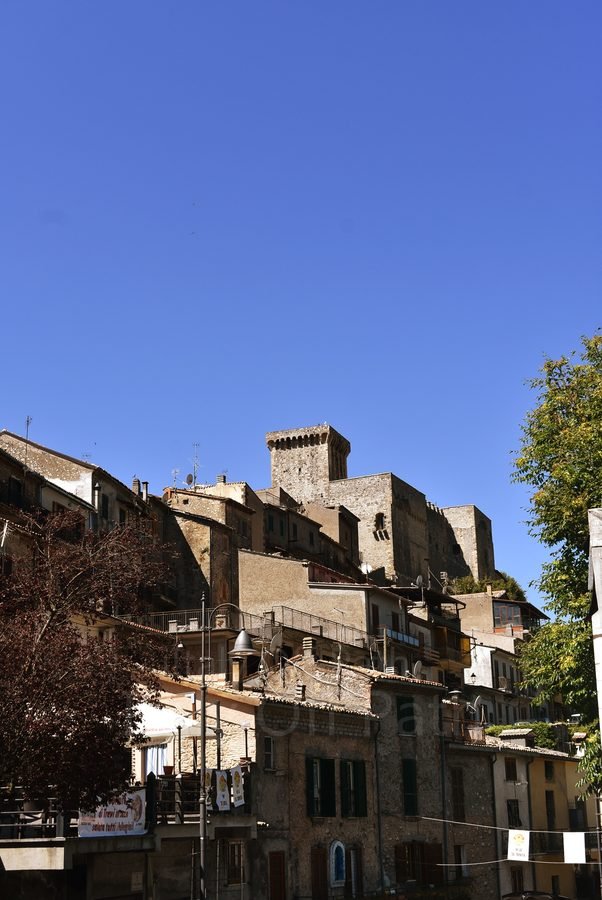Medieval stone houses rising toward the Castello Caetani fortress under a clear blue sky in Trevi nel Lazio, Italy.