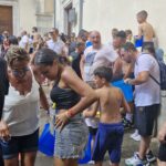Crowd of people, many wet and holding blue buckets, gathered in a narrow street during a water festival or celebration.