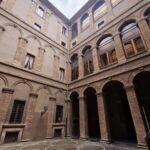Interior courtyard of a Renaissance palace with arched porticoes, decorative brickwork, and a patterned cobblestone floor.