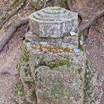Coins lie on a large stone, and above them towers something resembling an artifact with a piece of metal inside.