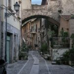 Wąska kamienna uliczka w Papigno z łukiem łączącym budynki.