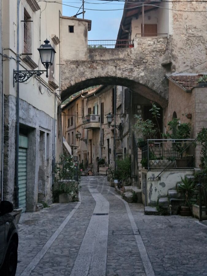 Wąska kamienna uliczka w Papigno z łukiem łączącym budynki.