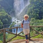 Female blonde Visitor standing at the panoramic viewpoint with Marmore Falls in the background in Umbria, Italy