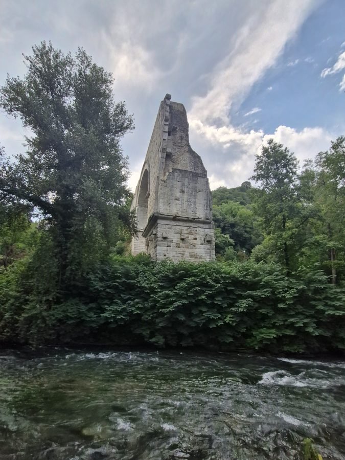 Surviving stone arch of the ancient Roman Ponte d'Augusto standing above dense vegetation on the bank of the Nera River in Narni, Umbria
