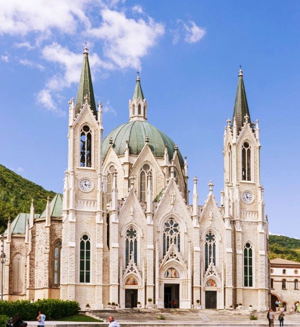 Neo-Gothic style church with twin spires, a large green dome, and pointed arches under a blue sky.