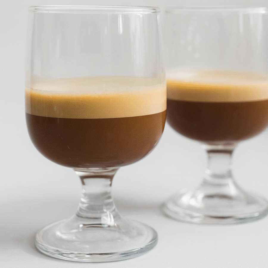 Two glasses of espresso with a thick layer of golden crema, placed on a light grey background.