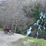 Waterfall in Italy cascading down mossy rocks in a forest, with a person sitting on a bench enjoying the peaceful view in winte