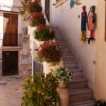 Stone staircase decorated with colorful potted flowers and wall art in a charming street of Polignano a Mare, Puglia.