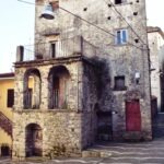 Historic stone building in an Italian village with arched balconies, weathered walls, and red wooden doors, photographed on a clear winter day.