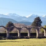 Stone arches of ancient ruins in Italy with snow-capped mountains in the background on a clear winter day