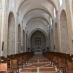 Interior of a Romanesque-style church in Italy with stone arches, vaulted ceilings, wooden pews, and a simple altar at the end of the nave