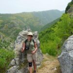 Hiker standing by a rock on a mountain trail with scenic valley views in Majella National Park.