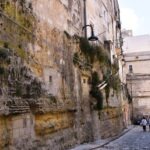 Narrow cobblestone street in Gravina di Puglia, Italy, with historic stone walls and old houses built directly into the rock