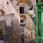 Stone stairway leading to historic houses carved into rock in Gravina di Puglia, Italy, with arched doorways and old stone walls
