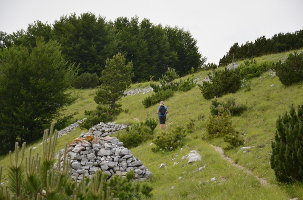 Hiker walking on a mountain trail in Majella National Park with stone cairn and green forest in Abruzzo