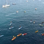People kayaking and paddleboarding in the Adriatic Sea near Polignano a Mare, Puglia, with boats anchored offshore