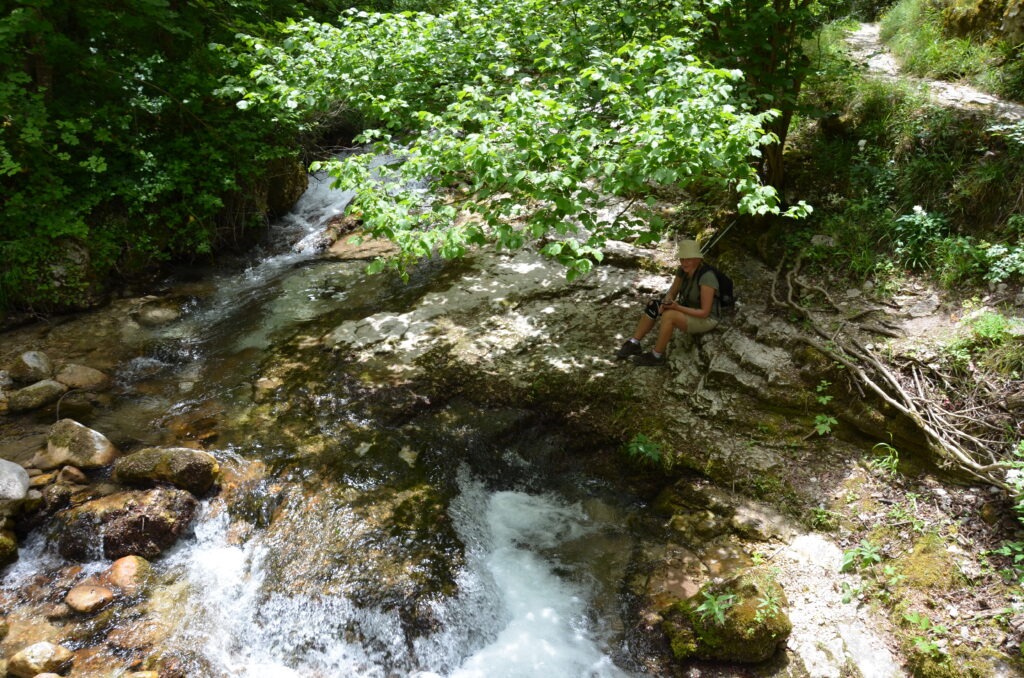 Kobieta odpoczywa nad górskim potokiem w dolinie Valle dell’Orfento w Parku Narodowym Majella – malownicze miejsce z krystalicznie czystą wodą i bujną zielenią w Abruzji.